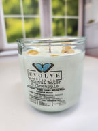 Coconut Water & Pineapple Rocks candle on a windowsill in daylight — tropical wood wick soy candle topped with golden healer quartz and yellow aventurine chips