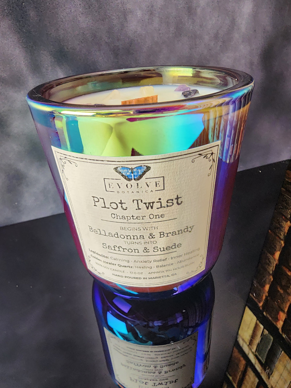 Close-up of Plot Twist Chapter One 12 oz layered candle label, Begins With Belladonna & Brandy, Turns Into Saffron & Suede, in iridescent glass