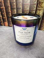 Plot Twist Chapter One 13.5 oz layered soy candle in iridescent black glass with wood wick and Lepidolite and Golden Healer Quartz, against antique leather-bound books