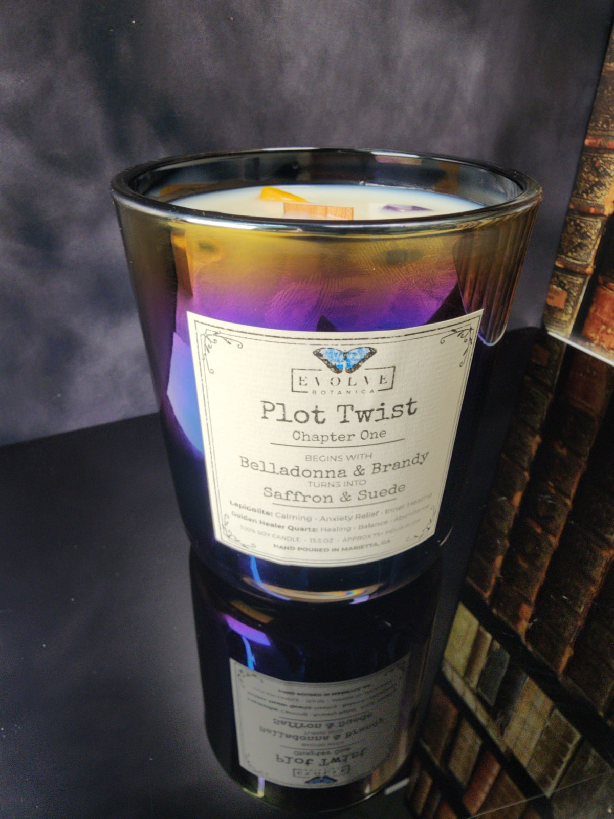 Plot Twist Chapter One 12 oz layered soy candle in color-shifting iridescent glass, Belladonna & Brandy turning into Saffron & Suede, wood wick topped with Lepidolite and Golden Healer Quartz