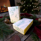 Silver Spruce hand and body soap bars on weathered wood with fresh spruce sprigs and gold ornaments near a crackling fire